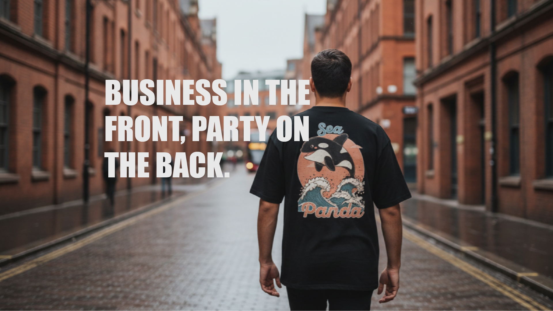 Person wearing a black t-shirt with a graphic design, walking down a city street with text 'Business in the front, party on the back'.