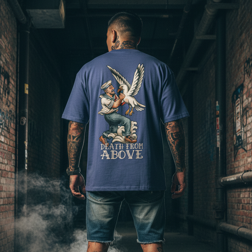 Man wearing a blue t-shirt with a tattoo graphic design and text, standing in a dimly lit alleyway.