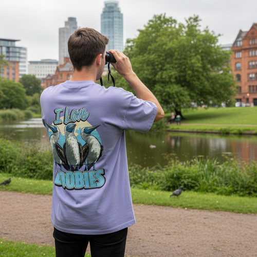 Man looking through binoculars in a park wearing a purple t-shirt with a graphic design.