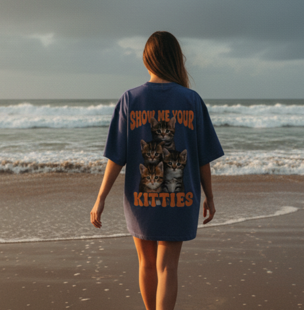 Person wearing a t-shirt with cat graphics and text on a beach